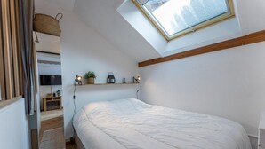 Une chambre à coucher avec une lucarne, un lit, une télévision et une étagère ornée d’objets décoratifs.