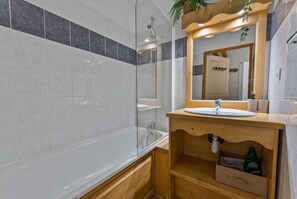 A modern bathroom with a glass-enclosed shower, a wooden vanity with a sink, and a mirror above the vanity. - Resort center, 3rd floor, fitness, swimming pool, sauna, balcony, fireplace or stove, tv, ski locker (Les Orres)