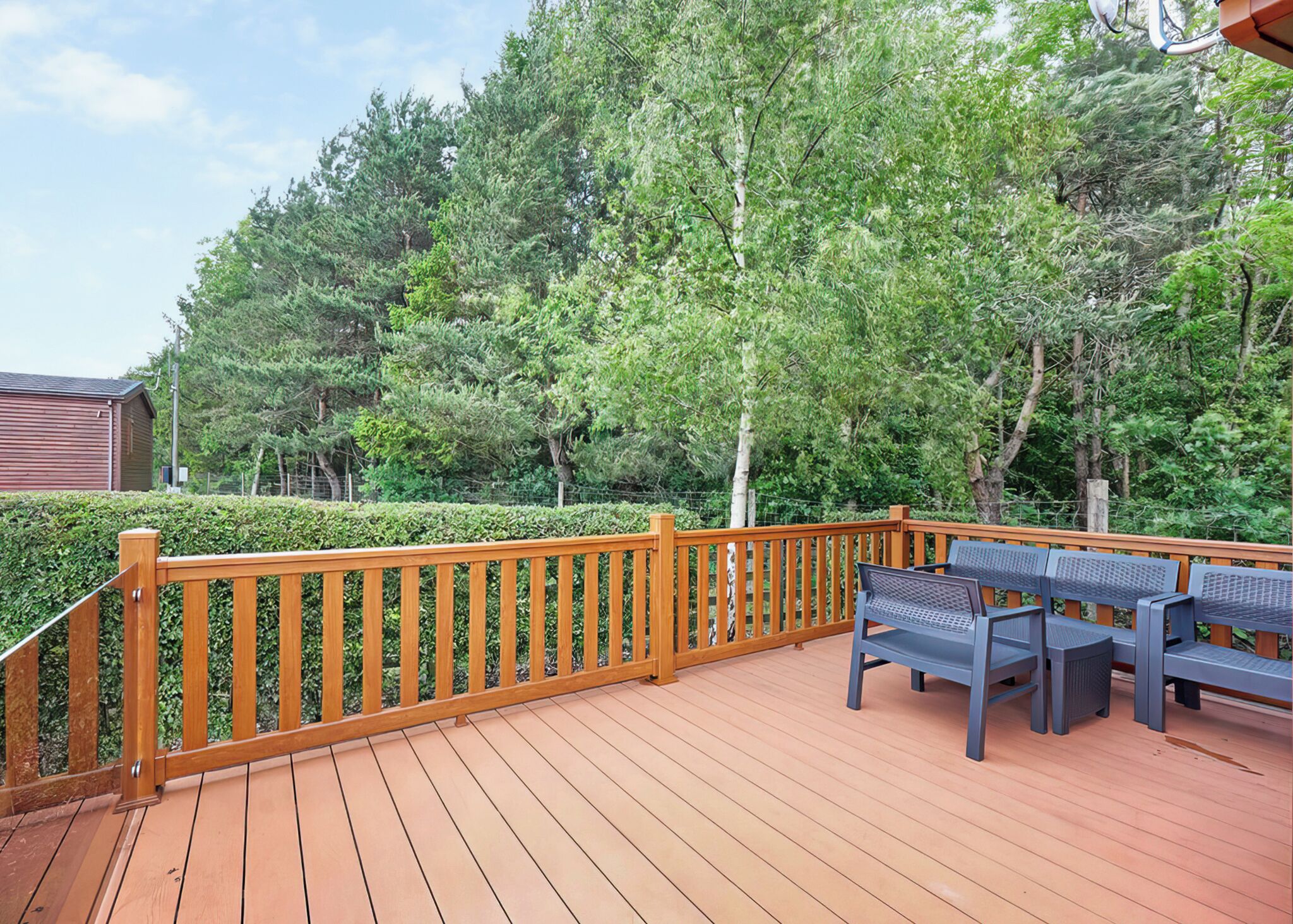 A wooden deck with a railing, benches, and a view of a forested area.