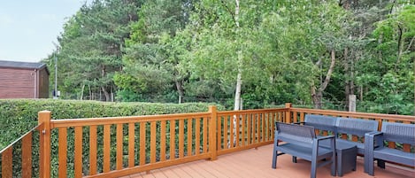 A wooden deck with a railing, benches, and a view of a forested area.