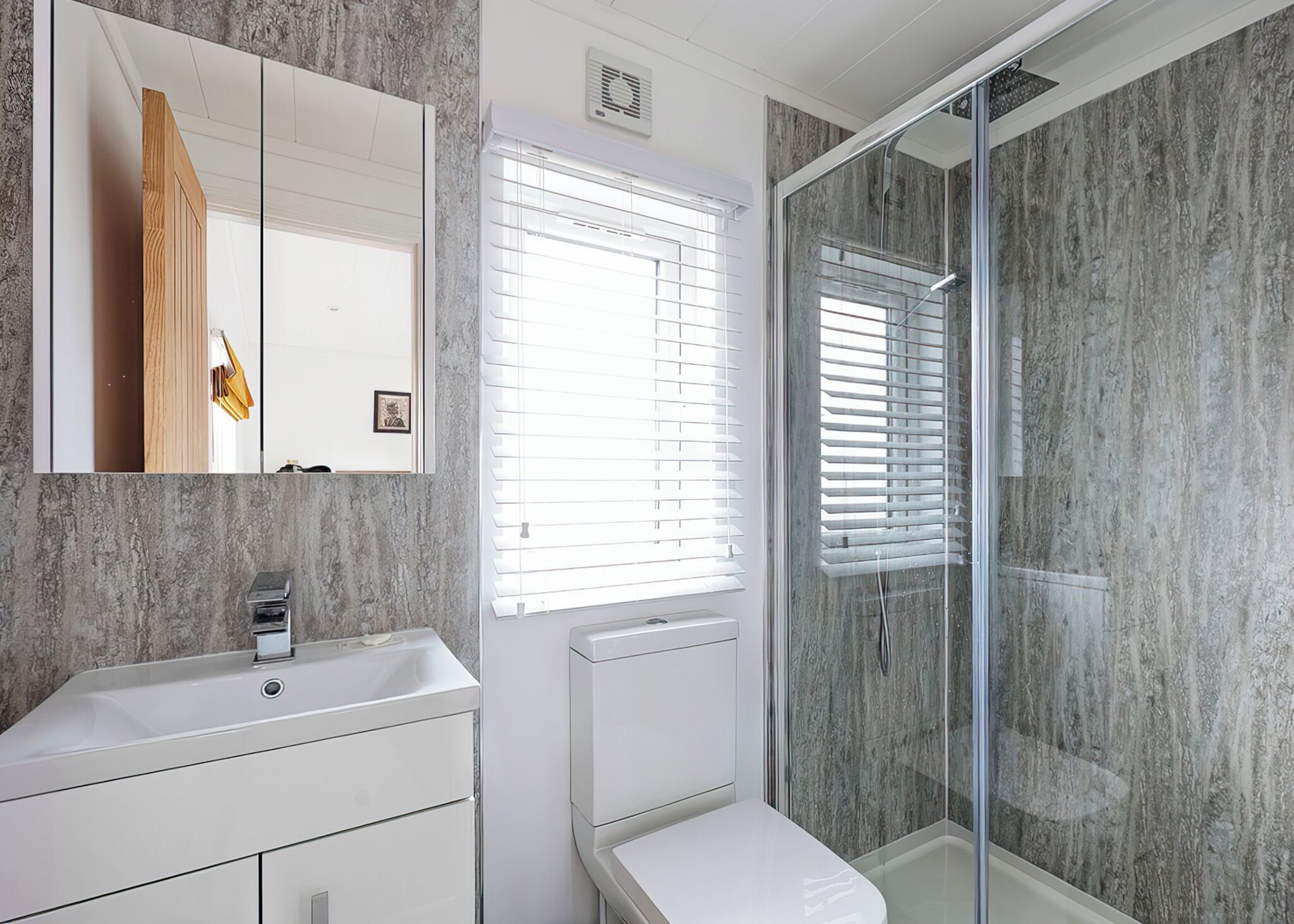 Une salle de bain moderne avec un mur en marbre, un lavabo blanc, un miroir et une cabine de douche en verre.