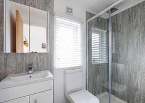 Un baño moderno con pared de mármol, un lavabo blanco, un espejo y una cabina de ducha con mampara de cristal.
