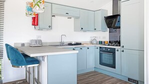 Une cuisine moderne avec des meubles de couleur bleu clair, un îlot central doté d’un tabouret de bar, un four encastré et un luminaire décoratif suspendu.