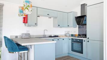 A modern kitchen with light blue cabinets, a central island with a bar stool, a built-in oven, and a hanging floral light fixture.