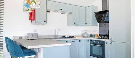 A modern kitchen with light blue cabinets, a central island with a bar stool, a built-in oven, and a hanging floral light fixture.