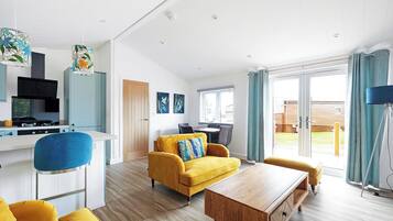 Un salon moderne avec un canapé jaune, une table basse en bois et un coin cuisine équipé d’une cuisinière et de placards.