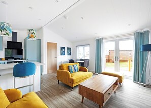 A modern living room with a yellow sofa, a wooden coffee table, and a kitchen area with a stove and cabinets.