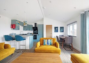 A modern kitchen with blue cabinets, a dining area with a table and chairs, and a living room with a yellow sofa and a coffee table.