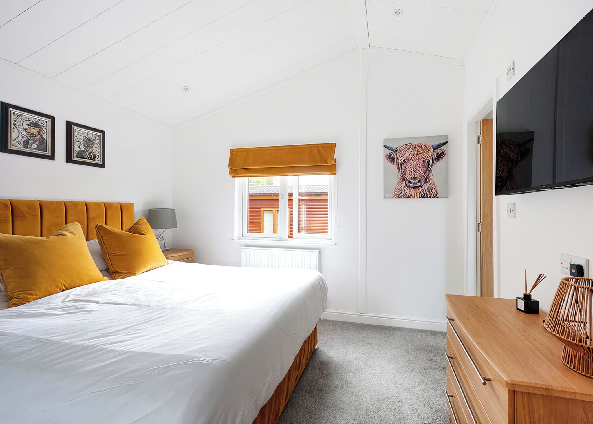A bedroom with a bed, a nightstand, a window with a view, a TV, and artwork on the wall.