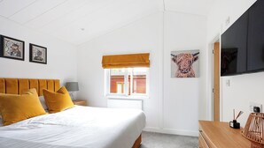 Une chambre à coucher avec un lit, une table de chevet, une fenêtre donnant sur un beau paysage, un téléviseur et des œuvres d’art accrochées au mur.