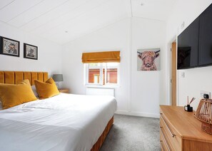 Een slaapkamer met een bed, nachtkastje, raam met uitzicht, televisie en kunst aan de muur.
