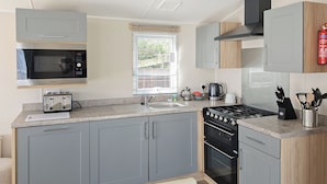 A modern kitchen with grey cabinets, a microwave, a toaster, a sink, a stove, and a window with blinds.