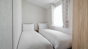 A small, clean room with two single beds, a wooden door, and a window with patterned curtains.