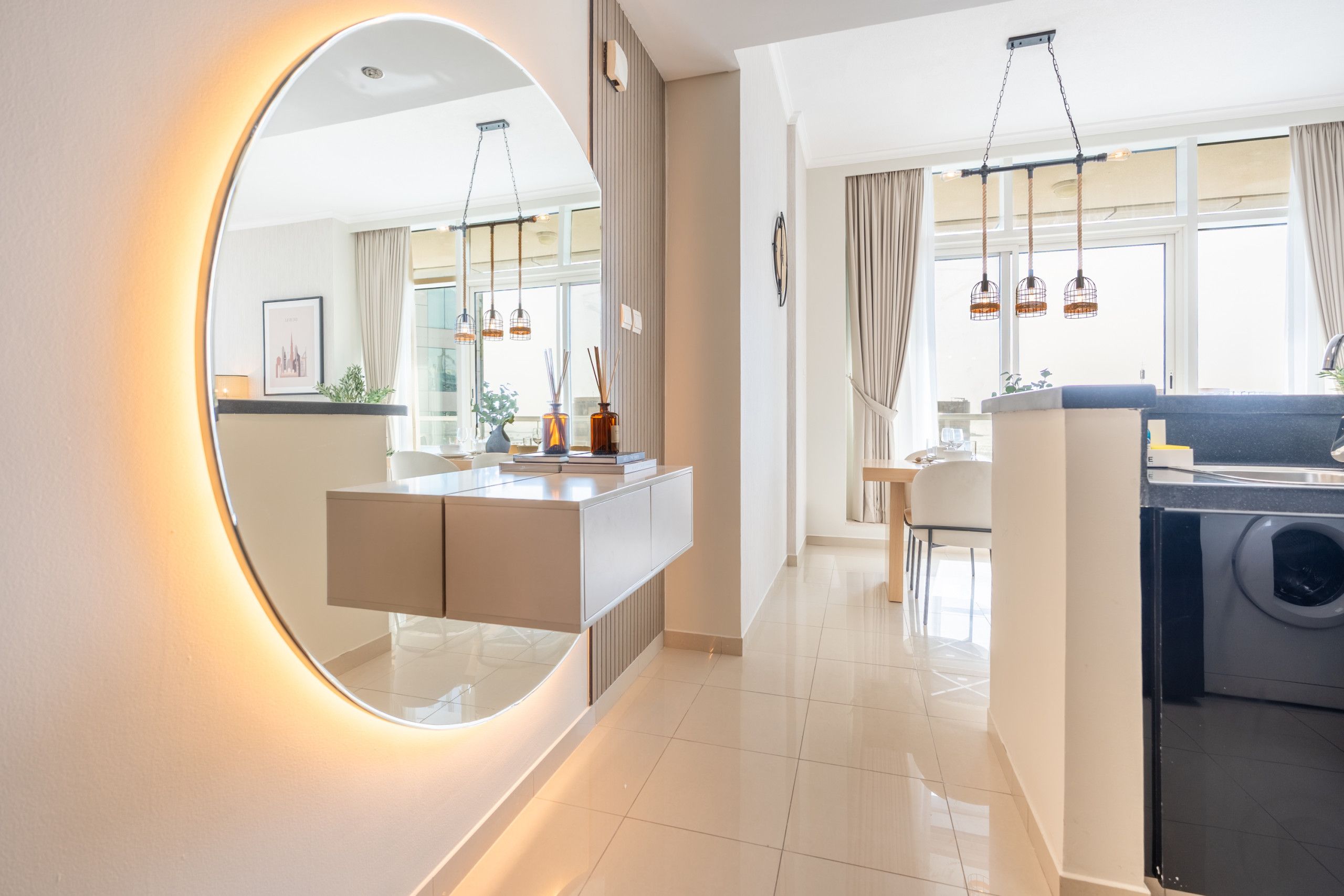 Een moderne keuken met een ingebouwde oven, een eethoek met een tafel en stoelen, en een grote spiegel met verlichting.