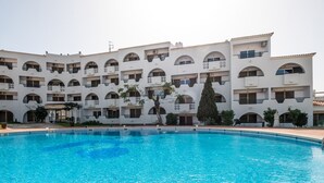 Ein Hotel mit einem großen Schwimmbad, mehreren Balkonen und einem Innenhof mit Bäumen.