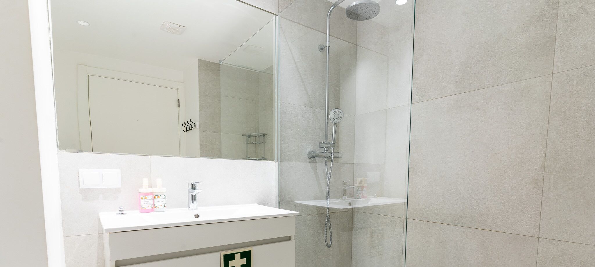 Une salle de bain moderne avec une douche à parois de verre, un meuble-lavabo blanc avec un miroir et une petite étagère.