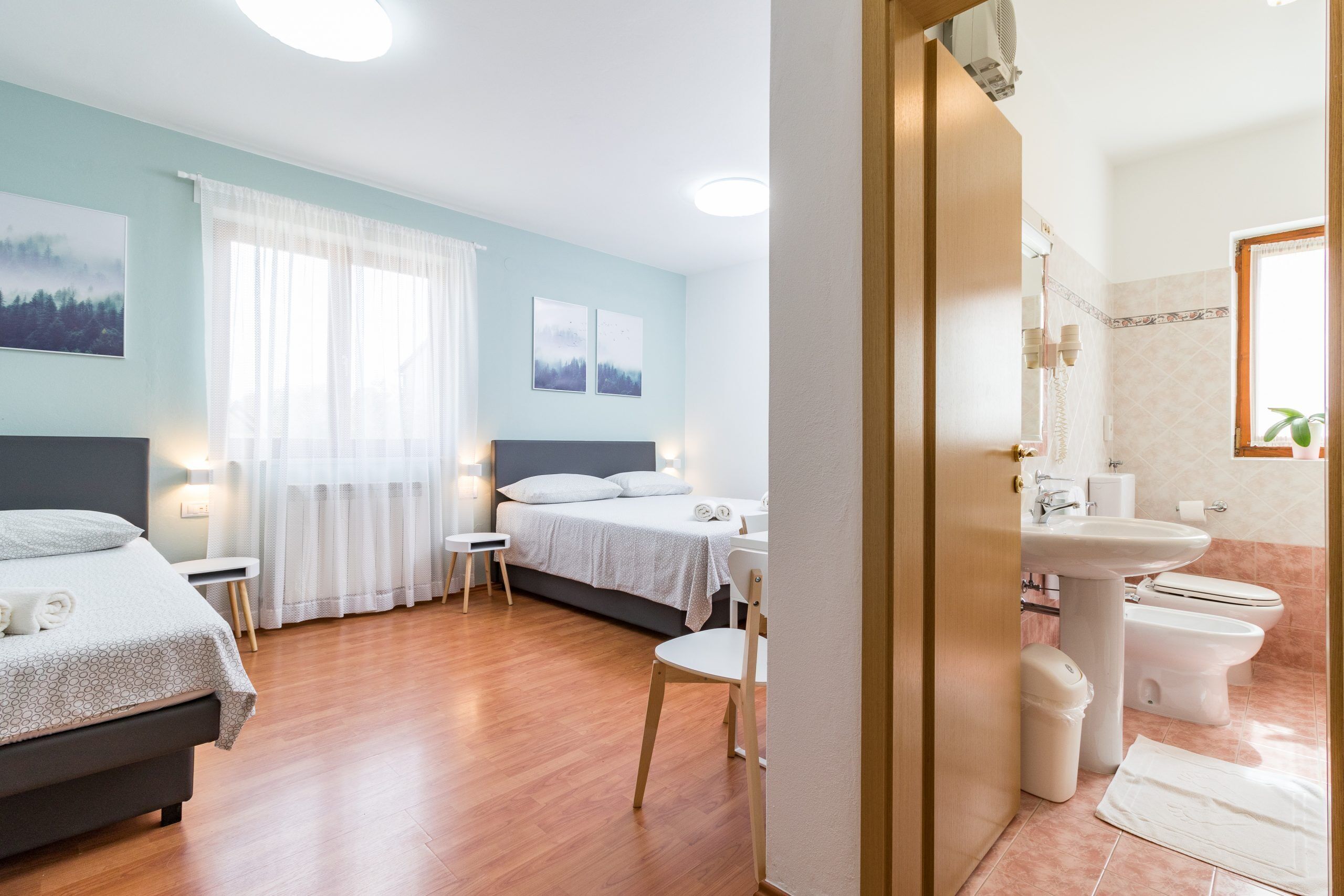 Une chambre d’hôtel avec deux lits, un coin salon, une salle de bain avec un lavabo et des toilettes, et une vue sur l’extérieur.