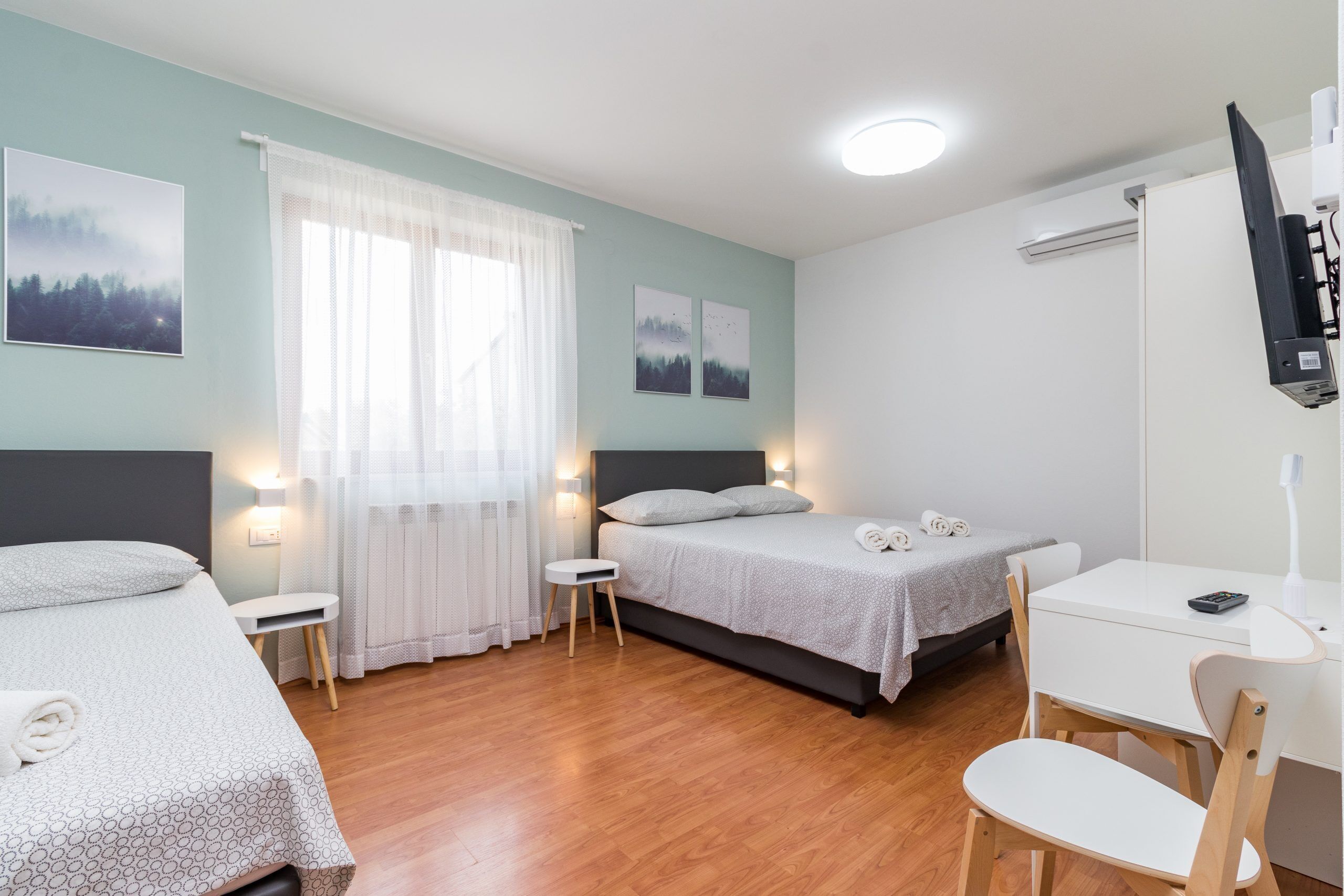 Una camera d'albergo con due letti, una scrivania, una sedia e una televisione.