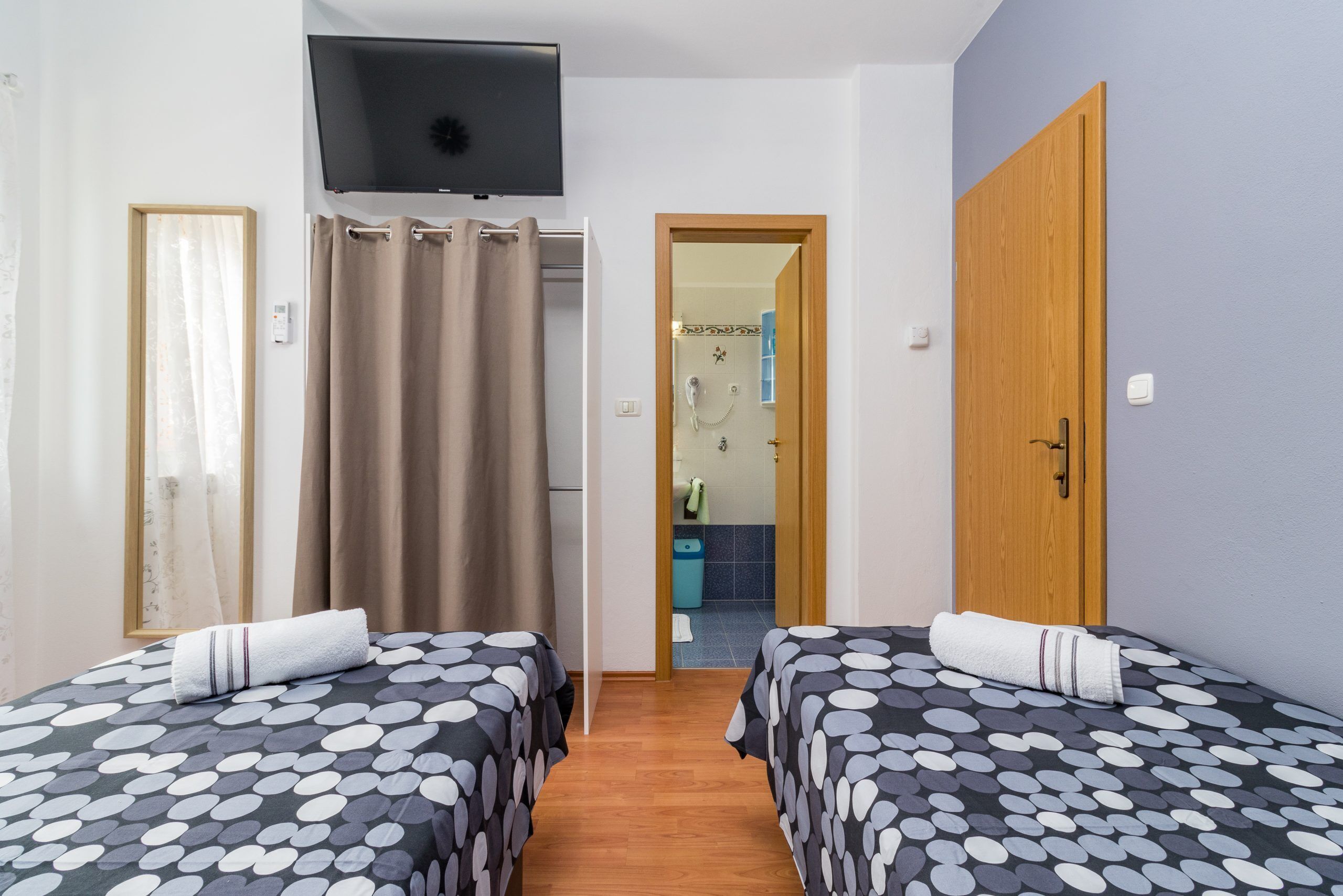 A hotel room with two beds, a TV, a shower, and a wooden door.
