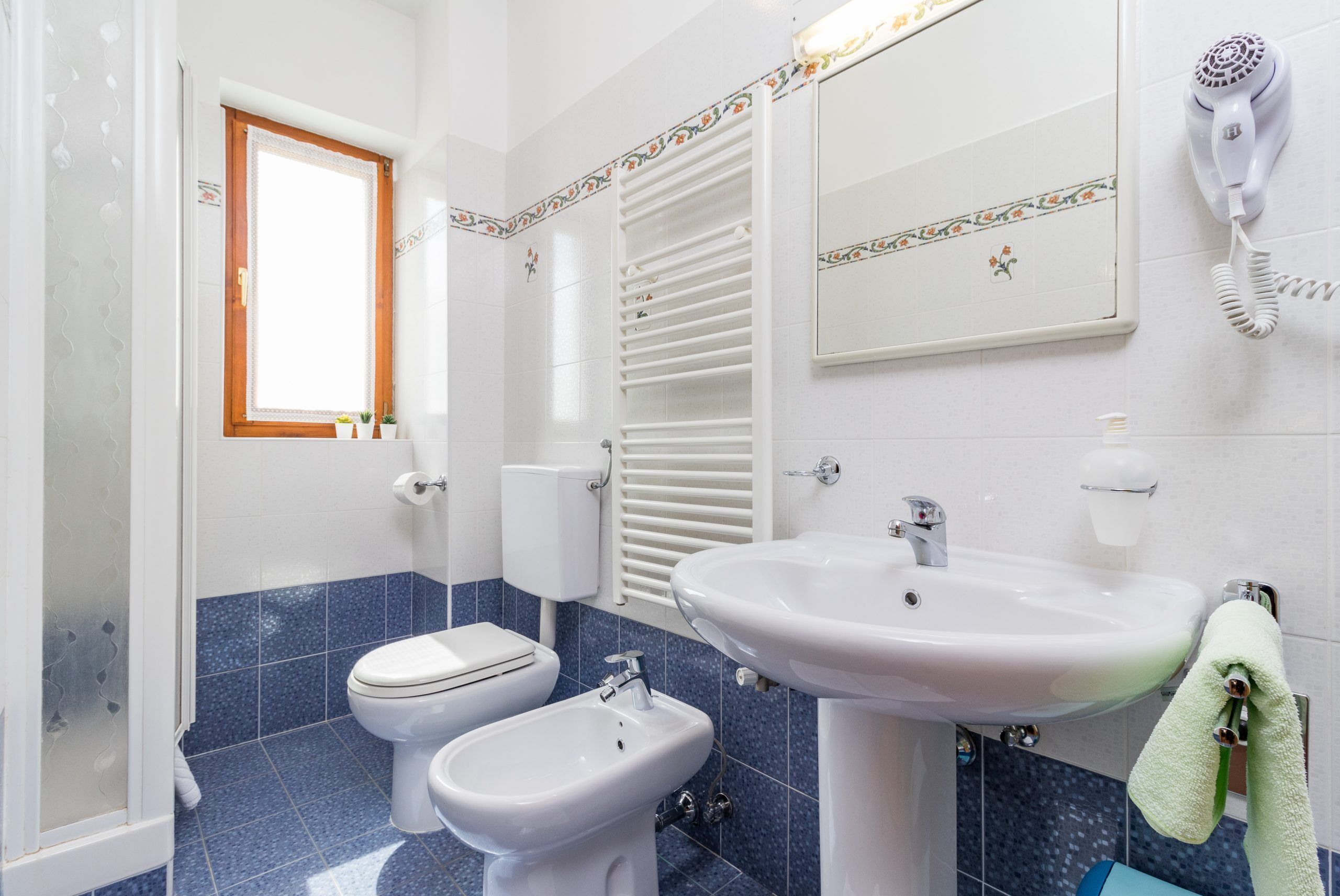 A bathroom with a toilet, bidet, sink, and a hairdryer on the wall.