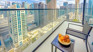 Un balcon situé dans un immeuble de grande hauteur, doté d’une balustrade en verre, une table avec des croissants et du jus d’orange, et une vue sur le paysage urbain.