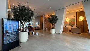 Un hall d’hôtel moderne, agrémenté de grands pots de plantes, d’un comptoir d’accueil et d’un mur orné d’un motif décoratif.