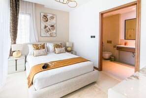 Ein modernes Schlafzimmer mit einem großen Bett, Nachttischen, einer Nachttischlampe, einem Wandbild und einem durchgehenden Türrahmen einsehbaren Badezimmer.