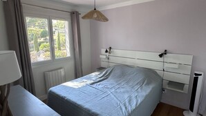Ein Schlafzimmer mit Bett, Schreibtisch, Stuhl, einem Fenster mit Vorhängen, einer Nachttischlampe und einer Heizung.