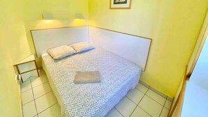 A small, single-bed room with a white headboard, a bedside table, and a framed picture on the wall.