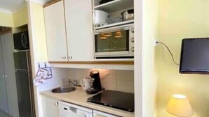 A compact kitchen with white cabinets, a coffee maker, a microwave, and a small sink.