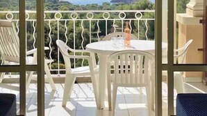 A balcony with a table and chairs, a bottle, and a view of the sea and greenery.