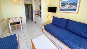 A compact living space with a sofa, a small dining table, a kitchenette, and a TV mounted on the wall.