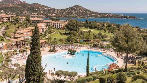 A resort with a large pool, multiple buildings, and a mountainous backdrop.