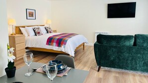 Ein Hotelzimmer mit einem Bett, einem grünen Sofa, einem Esstisch mit Tellern und Gläsern sowie einem an der Wand befestigten Fernseher.