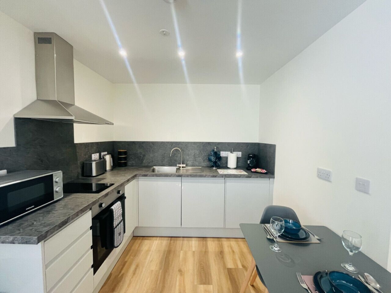 A compact kitchen with a microwave, toaster, sink, and a dining area with a table set for two.