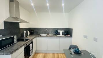 A compact kitchen with a microwave, toaster, sink, and a dining area with a table set for two.
