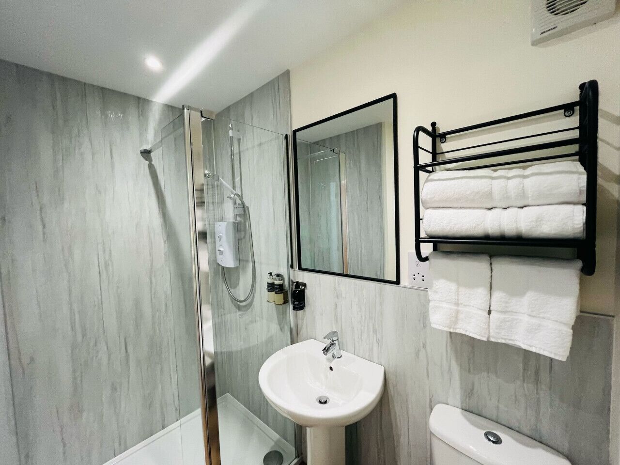 A modern bathroom with a glass-enclosed shower, a white sink, and a black towel rack.