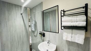A modern bathroom with a glass-enclosed shower, a white sink, and a black towel rack.