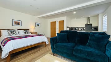 A bedroom with a bed, a teal sofa, and a kitchen area in the background.
