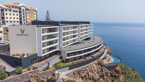 Ein modernes Hotel mit einem gebogenen Balkon mit Meerblick, das über mehrere Etagen und einen Poolbereich verfügt.