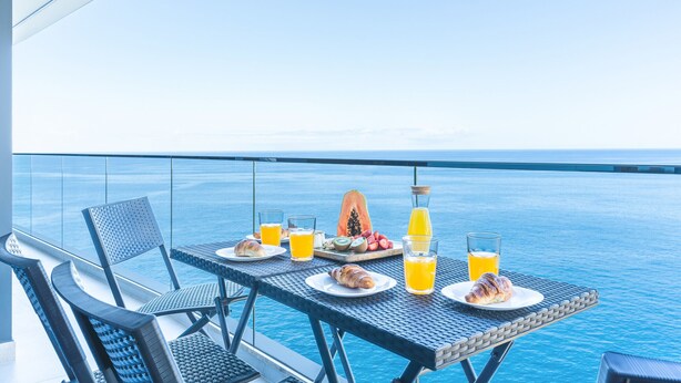 Ein Esstisch mit Frühstück und Getränken auf einem Balkon mit Meerblick.