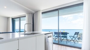 Eine moderne Küche mit Geschirrspüler, ein Essbereich mit Tisch und Stühlen sowie eine große Schiebeglastür, die auf einen Balkon mit Meerblick führt.