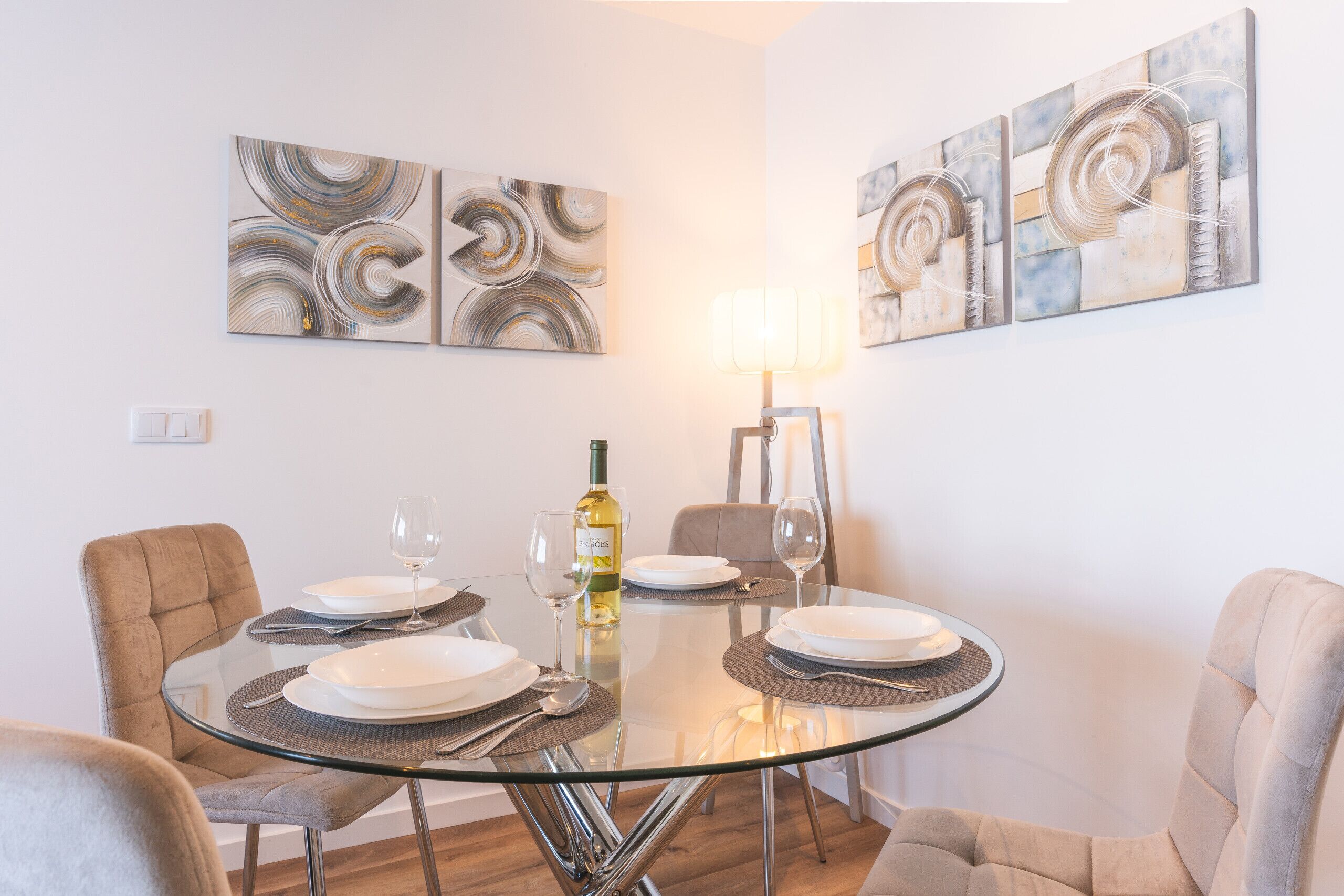 Un coin repas avec une table en verre, quatre chaises et deux tableaux abstraits accrochés au mur.