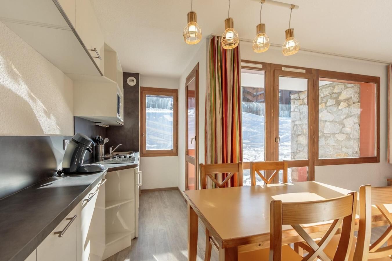 Cocina moderna con estufa, pileta y mesa de comedor de madera con sillas.