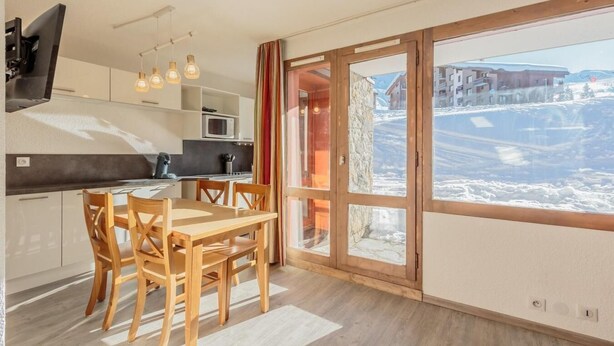 Una cocina moderna con comedor, ventanas amplias que dan a un paisaje nevado y una mesa de madera con sillas.