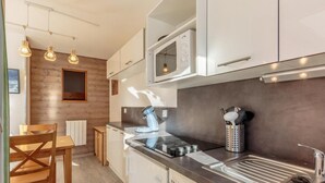 Una cocina moderna con microondas integrado, pileta de acero inoxidable y cafetera. Hay sillas de madera y una mesa de comedor, y la cocina tiene un muro decorativo de madera.
