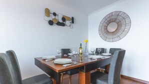 Een eetruimte met een houten tafel voor zes personen, gestoffeerde grijze stoelen, een decoratief wandobject en een grote spiegel.