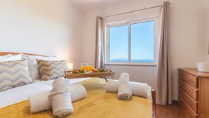 Hotelkamer met een bed, een houten dressoir, een raam met gordijnen, en een dienblad met handdoeken en fruit.