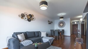 Een moderne woonkamer met een grijze hoekbank, een zwarte salontafel en een eethoek met een ronde tafel en stoelen.