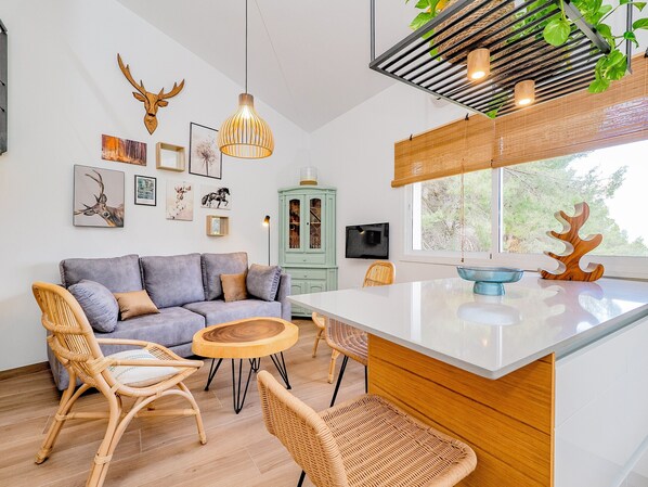Una sala de estar moderna con un sofá gris, sillas de mimbre, una mesa de centro de madera y un ventanal con vistas a árboles.